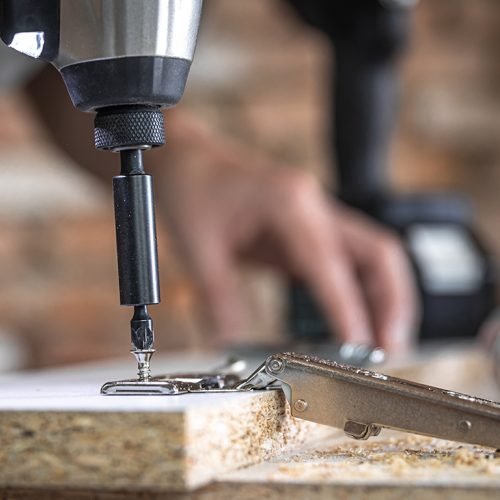 Screwing a self-tapping screw into a metal fastening hole on a wood strip using a screwdriver, the work of a carpenter.