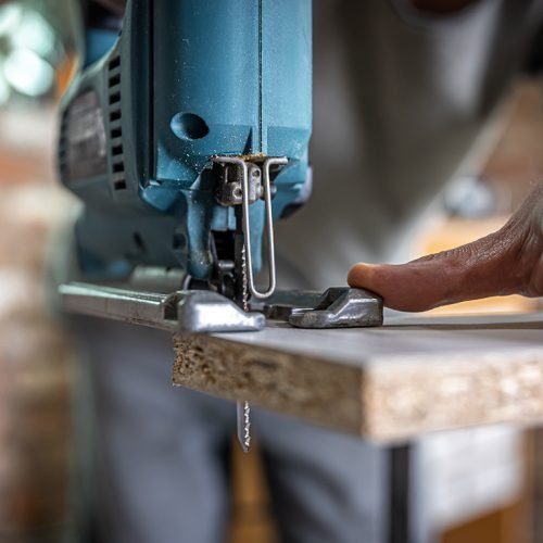 A male carpenter cuts a wood with an electric jigsaw, working with a tree.